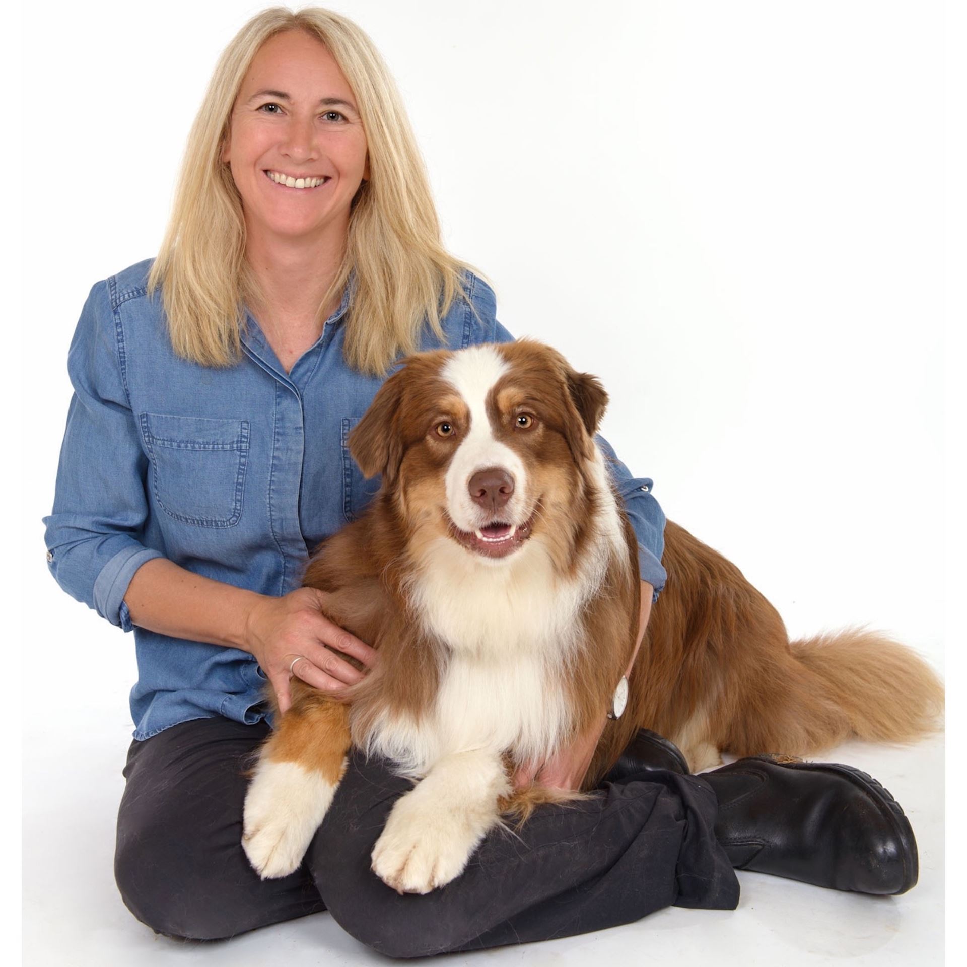 Alexis Davison and her dog Arlo look at the camera while in relaxed poses. Alexis has blond hair and is wearing a blue shirt and pants. Arlo is a trie coloured Australian Shepard